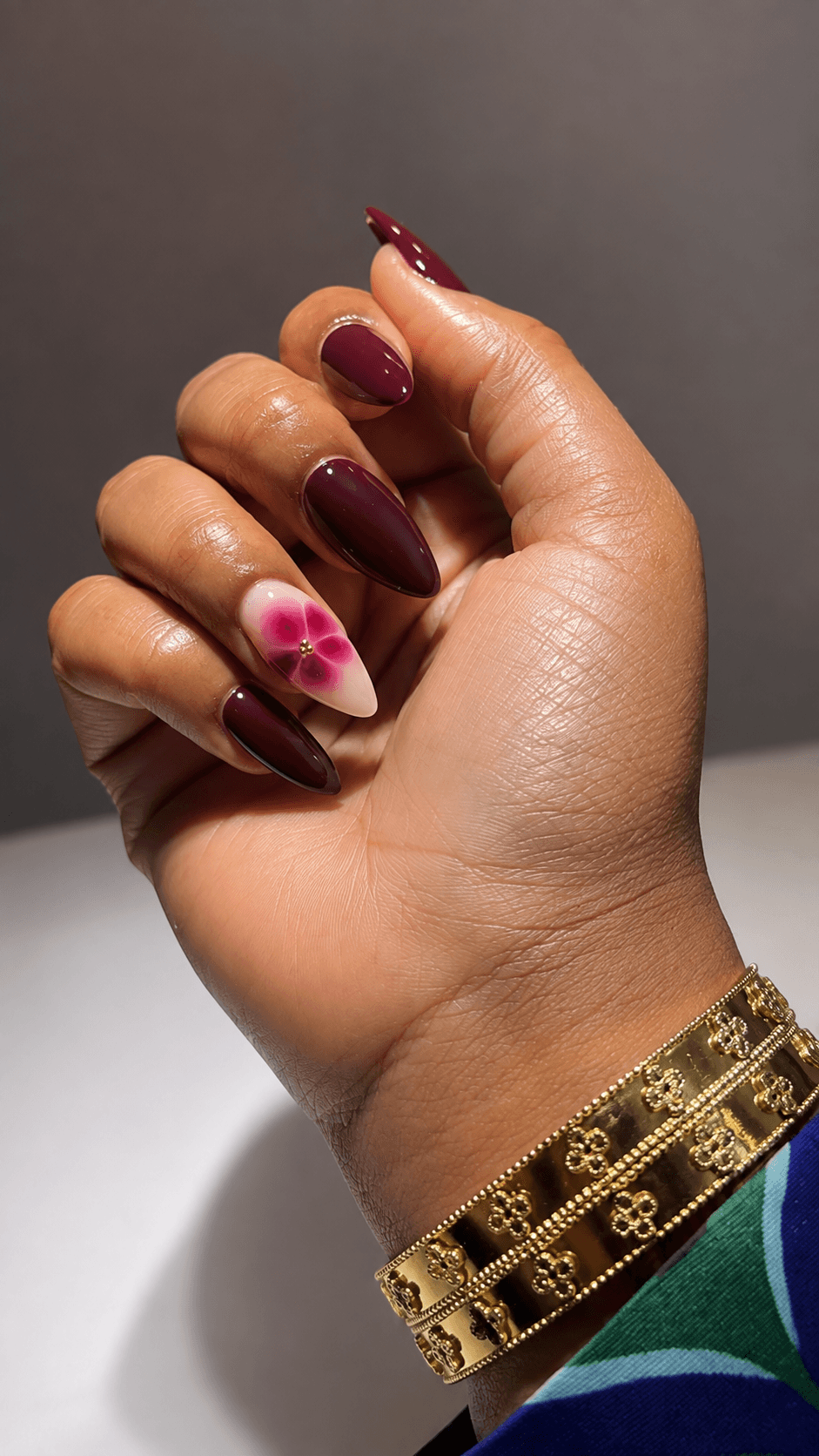 Ongles amande bordeaux ornés d’un nail art floral rose.