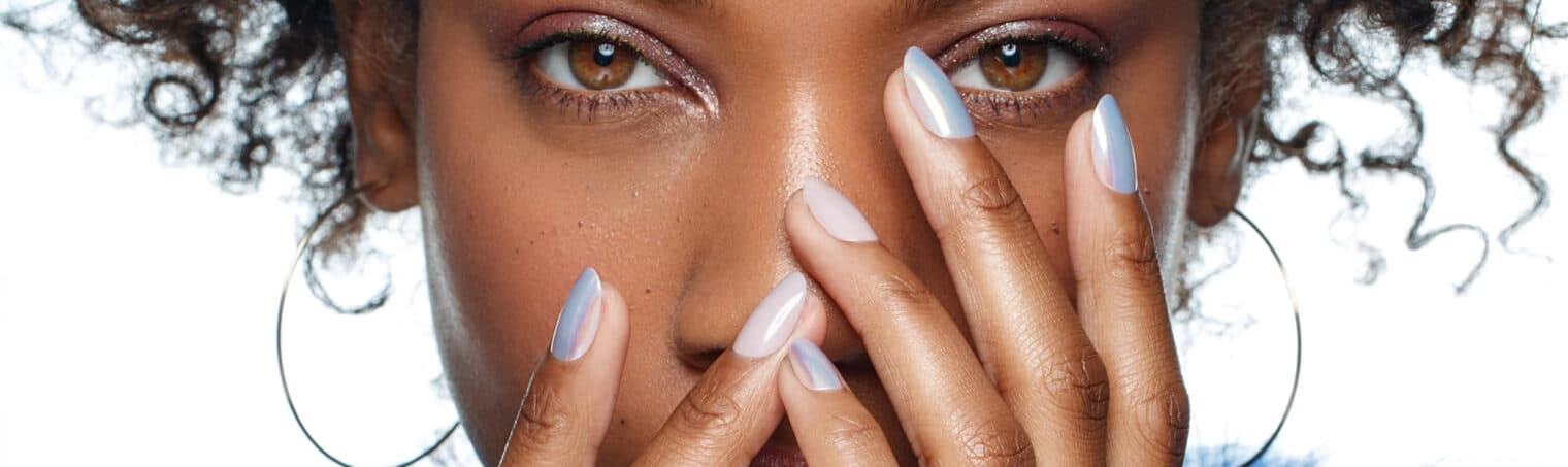 Gros plan sur des ongles amande en dégradé de bleu pâle, les mains posées devant le visage.